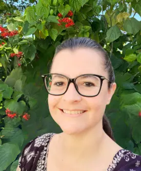 Mujer sonriendo con gafas frente a un fondo de plantas verdes y flores rojas, representando a los consejeros del Sunshine State Counseling Center en Bonita Springs, FL.