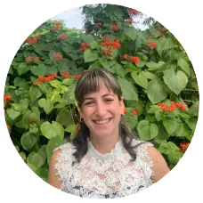 Elizabeth Martin, LMHC, smiling in front of vibrant green foliage and orange flowers, representing the Sunshine State Counseling Center's team of therapists.