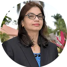 Suganya Rathod, MA, therapist at Sunshine State Counseling Center, standing outdoors in a professional outfit with a blurred background of tropical plants.