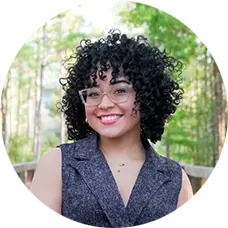 Karinna Chaluisant, MSW, therapist at Sunshine State Counseling Center, smiling outdoors with curly hair and glasses, surrounded by greenery.