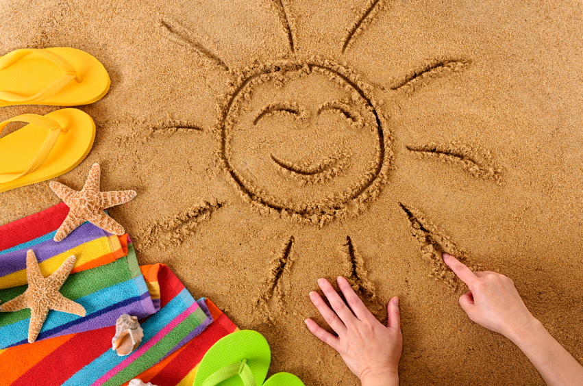 Child drawing a smiling sun on a sandy beach, with beach towel, starfish and flip flops (studio shot - warm color and directional light are intentional).